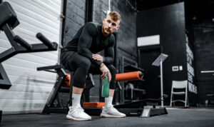 a man sitting on a bench in a gym and holding a green water bottle
